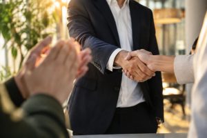 Poignée de main entre deux professionnels sous les applaudissements, symbolisant la réussite d'un accord financier.
