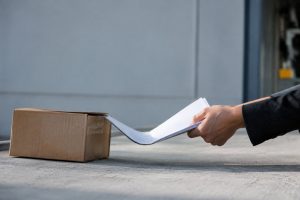 Une main en costume retire un document d'un carton posé au sol.