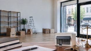Bureau avec une maquette de magasin, des documents juridiques et une balance de justice devant un local vide.